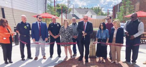 Above, City of Rossford and TARTA representatives cut the ribbon on the completed park. Below right, the pocket park features picnic tables with umbrellas, turf, a water feature and string lighting.