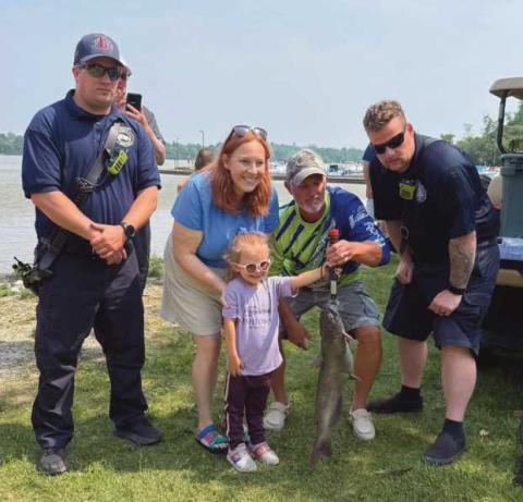 Tessa Sutter (front), the winner of Rossford’s 2025 Cops and Bobbers event, poses with her catch, a 7.9 pound channel catfish. Bass Pro, a sponsor of the event, congratulated her on her catch by gifting her a hat, fishing pole and tackle box. “She might be six inches taller than the fish,” commented Rossford Police Chief Todd Kitzler (helping her hold the fish in the picture), who said the Cops and Bobbers event is one of the most enjoyable things he gets to do.