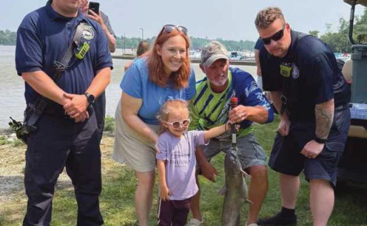 Tessa Sutter (front), the winner of Rossford’s 2025 Cops and Bobbers event, poses with her catch, a 7.9 pound channel catfish. Bass Pro, a sponsor of the event, congratulated her on her catch by gifting her a hat, fishing pole and tackle box. “She might be six inches taller than the fish,” commented Rossford Police Chief Todd Kitzler (helping her hold the fish in the picture), who said the Cops and Bobbers event is one of the most enjoyable things he gets to do.