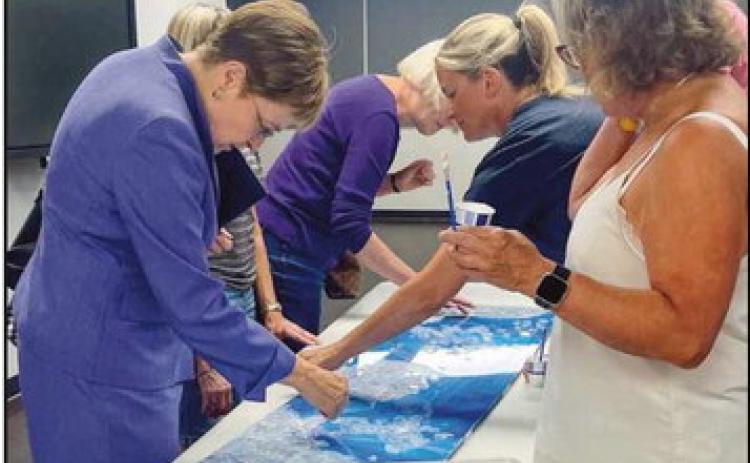 U.S. Congresswoman Marcy Kaptur places a piece of LOF glass in the mosaic as artist Gail Christofferson looks on, at Rossford’s 125th celebration at Rossford High School.
